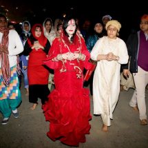 Radhe Maa in a red mermaid outfit - replete with a red purse and surrounded by devotees