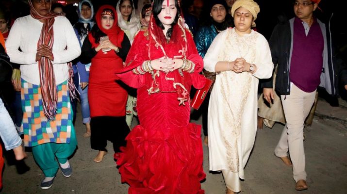 Radhe Maa in a red mermaid outfit - replete with a red purse and surrounded by devotees